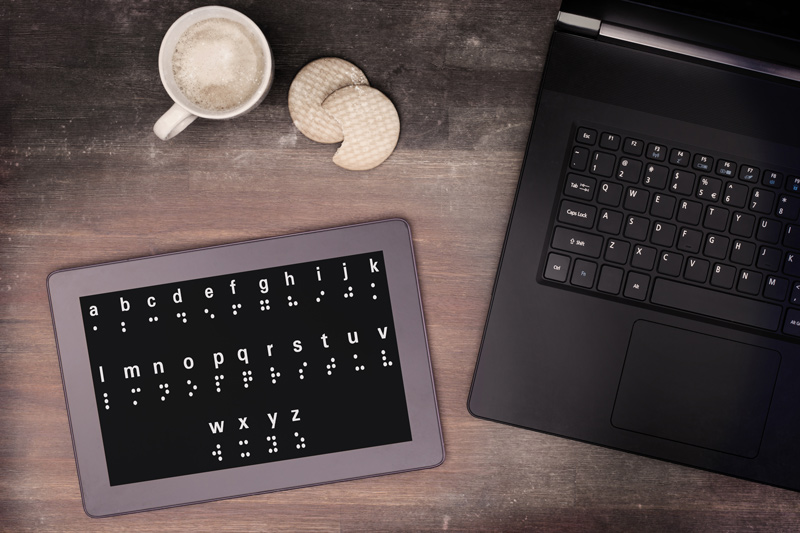A tablet with braille characters next to an open laptop