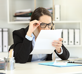 Woman wearing glasses, squinting to read a document.